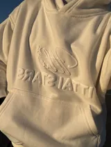 Buzo hoodie color crema con bolsillo tipo canguro y logo de la marca bordado en el frente.