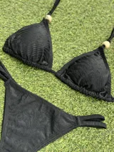 Bikini negra con corpiño triangular que tiene un aplique de piedra en el bretel y bombacha colaless con tiras ajustables laterales.