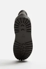 Bota de cuero color marrón oscuro con cordones amarillos, estilo trekking, con suela de goma con volumen.