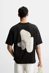 Camiseta negra de corte holgado con cuello redondo y mangas cortas. Estampado frontal con la frase "Unfolding Dreams" en letras blancas.