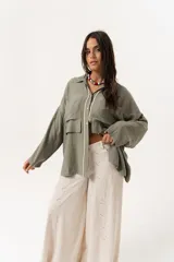 Camisa verde militar de manga larga con silueta oversize, dos bolsillos delanteros y corte levemente más largo en la espalda. Escote en V abotonado con detalle de galón picot a lo largo de la cartera y botones a tono. Isotipo bordado en la parte trasera.