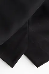 Short pollera negro de tiro alto con diseño cruzado tipo pareo y cinturón fijo con hebilla revestida. Presenta cierre oculto y cierre de corchete en un lateral.