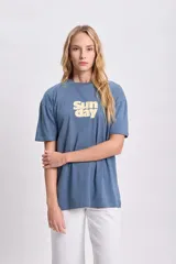 Remera celeste de corte amplio con estampa amarilla con la palabra 'Sunday'.