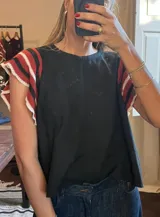 Top negro de corte holgado con mangas cortas tejidas a rayas rojas, negras y blancas, con borde festoneado.