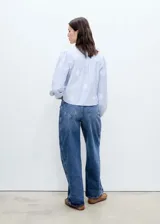 Camisa celeste a rayas verticales con bordado floral blanco, cuello camisero, manga larga abullonada y cierre frontal con botones.