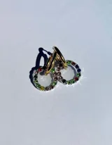 Par de aros colgantes con argollas doradas y dijes circulares de resina transparente con incrustaciones de strass de colores. El dije mide aproximadamente 1.5cm de diámetro.