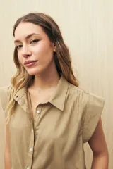 Camisa color beige, de corte recto, con cuello clásico, mangas cortas con volados en los hombros y cierre frontal con botones.