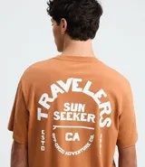 Remera masculina color marrón, de corte comfort, con cuello redondo y mangas cortas. Presenta un estampado de letras "Travelers" en el pecho y la espalda.
