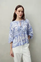 Blusa estampada celeste y blanca de caída fluida con cuello redondo y lazos frontales. Diseño con cortes horizontales y frunces, mangas largas con puños elastizados.
