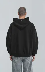 Hoodie negro de corte oversize con capucha, bolsillo tipo canguro y detalle de bolsillo con cierre en la manga izquierda.