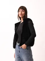 Chaleco negro de textura afelpada o pelo sintético, con cierre frontal.