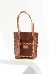 Bolso tipo tote de cuero marrón con textura croco y asas color suela. Tiene un bolsillo externo con aplique de cuero con el logo de la marca y un colgante de flecos de cuero.