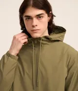 Campera rompevientos color verde oliva, con capucha ajustable con cordón, cierre frontal con cremallera, bolsillos laterales con cremallera y puños elásticos.