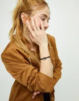 Pulsera de cuero negro con dije central de cristal facetado gris y detalles en metal dorado.