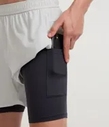 Short deportivo para hombre, color gris claro, con short de compresión negro incorporado. Presenta un pequeño logo bordado en la pierna derecha.