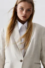 Blazer color beige de lino y viscosa, con solapas de pico, hombreras finas, cierre de un botón, pinzas en la cintura, abertura con botón en los puños, bolsillos delanteros ribeteados y abertura atrás.