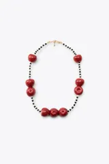 Collar corto con cuentas pequeñas blancas y negras, y dijes grandes de cerezas rojas. Cierre de mosquetón dorado.