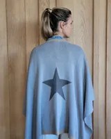 Ruana negra de tejido de punto con una estrella grande color beige en la espalda y borde inferior con franja beige.