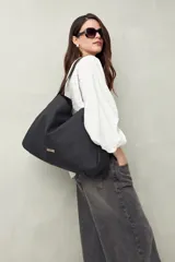 Bolso negro amplio tipo tote bag, confeccionado en poliuretano, con líneas minimalistas y diseño versátil.