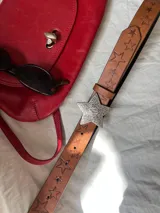 Cinturón marrón de cuero sintético con estrellas grabadas y hebilla plateada en forma de estrella.