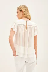 Camisa azul de algodón liviano con cuello redondo y gota en la espalda. Presenta detalle de bordado calado, terminación de volado en mangas y ruedo.