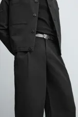 Pantalón negro relaxed fit confeccionado en tejido con algodón, lino y lyocell. Cintura con detalle de pliegues frontales dobles, bolsillos delanteros y traseros. Cierre frontal con cremallera y botón.
