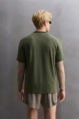 Camiseta deportiva verde militar confeccionada en tejido estructurado, ligero y elástico. Tiene cuello redondo, manga corta y bajo con aberturas laterales. Incluye logo estampado en el bajo.