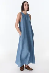 Vestido largo de lino color celeste, corte amplio y sin mangas, con ruedo desflecado y bolsillos laterales.