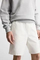 Bermuda color verde militar de corte relajado, confeccionada en tejido de algodón. Tiene cintura elástica ajustable con cordón interior, bolsillos frontales y bolsillo trasero de parche.