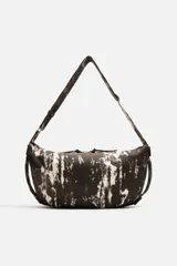 Bolso de hombro tipo bandolera, confeccionado en tejido de algodón con estampado abstracto en tonos blanco y negro. Cuenta con un compartimento principal con cierre de cremallera, un bolsillo interior con cremallera y asa de hombro ajustable.