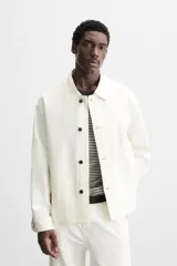 Sobrecamisa color crudo de corte boxy fit, confeccionada en tejido de algodón denim con estructura irregular. Tiene cuello solapa, manga larga con puños abotonados, bolsillos de vivo en la cadera y cierre frontal con botones.