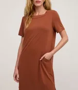 Vestido corto marrón, estilo camiseta, con escote redondo, mangas cortas y bolsillos laterales. El bajo es redondeado.