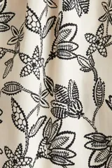 Vestido midi color crudo con estampado de hojas en negro, breteles finos ajustables y escote recto con frunces.