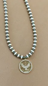 Collar corto de cuentas blancas y negras alternadas, con dije redondo dorado con diseño de espíritu santo.