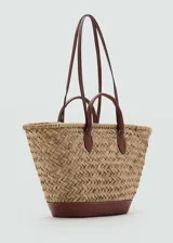 Bolso tipo canasta de paja trenzada color beige con base y asas cortas de cuero marrón. Incluye bolsa de tela interior y cierre con nudo.