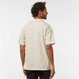 Remera tipo polo color beige claro, de manga corta y corte holgado.