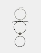Set de tres pulseras flexibles plateadas: una con strass, una de cadena de eslabones y una con dije de flor metálica.