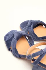 Sandalia de terciopelo verde con taco cuadrado de 7 cm, punta cuadrada y tiras anchas anudadas en el empeine. Cuenta con una tira fina ajustable al tobillo con hebilla dorada.