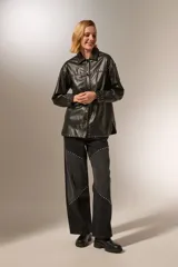 Chaqueta negra de eco-cuero con cuello camisero, corte holgado, cierre con broches y tachas plateadas.