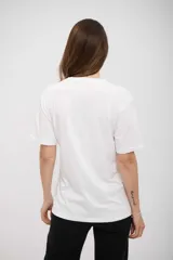 Remera blanca de manga corta con cuello redondo y un estampado frontal abstracto que simula una pincelada grande con base dorada y bordes negros.