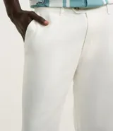 Pantalón de vestir blanco, de corte recto, con bolsillos laterales y traseros. Se ajusta a la cintura con cinturón de cuero marrón.