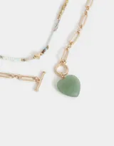 Collar corto doble con cadena dorada de eslabones rectangulares y cadena de mostacillas de colores con dije de corazón dorado y dije de piedra verde en forma de corazón.