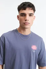 Remera oversize azul con estampado en la espalda de una flor abstracta en tonos rosa y amarillo sobre un fondo azul oscuro.