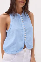 Top sin mangas color beige, con escote en V y cierre frontal de botones de nácar. Presenta costuras decorativas en el borde del escote y sisas.