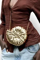 Bolso con forma de caracola color dorado, con efecto metalizado y asa de cadena.