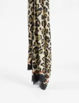 Pashmina rectangular con estampado animal print en tonos beige, marrón y negro. Tiene un borde negro liso y un detalle lineal marrón.
