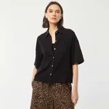 Camisa negra de lino con corte holgado, cuello clásico, manga corta y cierre frontal con botones.