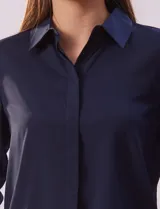 Camisa blanca de gasa, marca Sioni, con cuello con solapa, abertura central con botones y mangas largas con puño y botón.