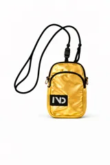 Cartera bandolera pequeña color dorado metálico, con cierre principal y bolsillo frontal con cierre. Tiene una correa ajustable de cordón negro y un parche rectangular negro con el logo "IND" en blanco.