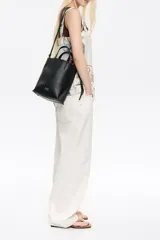 Bolso de mano mediano marca Bimba y Lola, color naranja, confeccionado en cuero con textura granulada. Tiene doble asa corta, correa bandolera ajustable y extraíble, logo estampado en el frente y herrajes plateados. El interior cuenta con etiqueta de tejido con el logo de la marca.